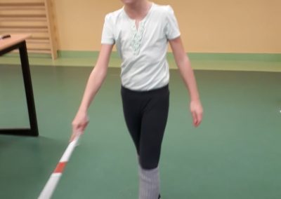 Dziewczynka w sali gimnastycznej przechadza się z goglami na oczach oraz białą laską