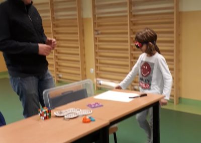 Tomasz tłumaczy uczennicy jak poruszać się z białą laską. Zajęcia w sali gimnastycznej. Przed Tomaszem stoją ławki na których leżą przyrządy do warsztatów